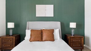 Ein Bett mit grauem Kopfteil, zwei Nachttische mit Lampen und eine grüne Wand.