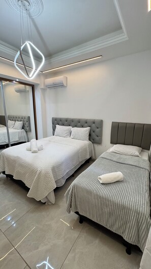 A modern bedroom with two beds, a large mirror, and a unique geometric light fixture. - 4 Suite apartment in Copacabana Rio de Janeiro One block from the beach (Rio de Janeiro)