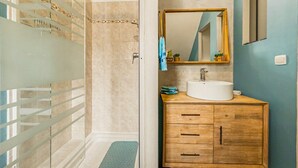 A bathroom with a shower, a sink, and a wooden cabinet. - Le Cocon du Bénitier - plage et lagon (Saint-Paul)