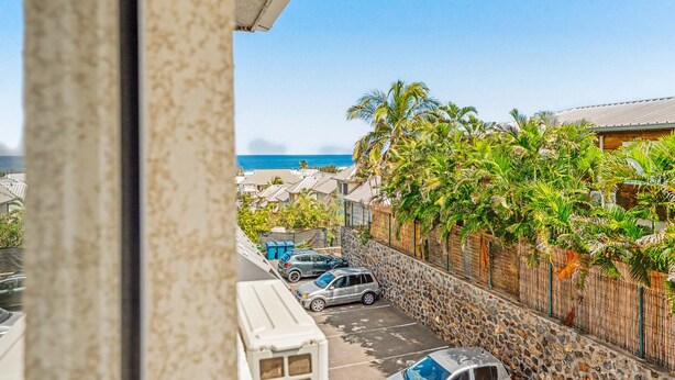A residential area with a view of the ocean, parked cars, and a stone wall with vegetation. - Le Cocon du Bénitier - plage et lagon (Saint-Paul)
