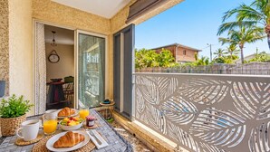 A balcony with breakfast items, a view of a house, and palm trees. - Le Cocon du Bénitier - plage et lagon (Saint-Paul)