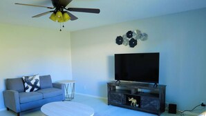 Uma sala de estar com sofá, mesa de centro, televisão e ventilador de teto.