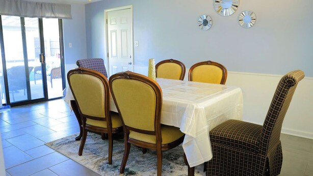 Uma sala de jantar com uma mesa posta para quatro pessoas, um ventilador de teto e uma porta que dá para o exterior.