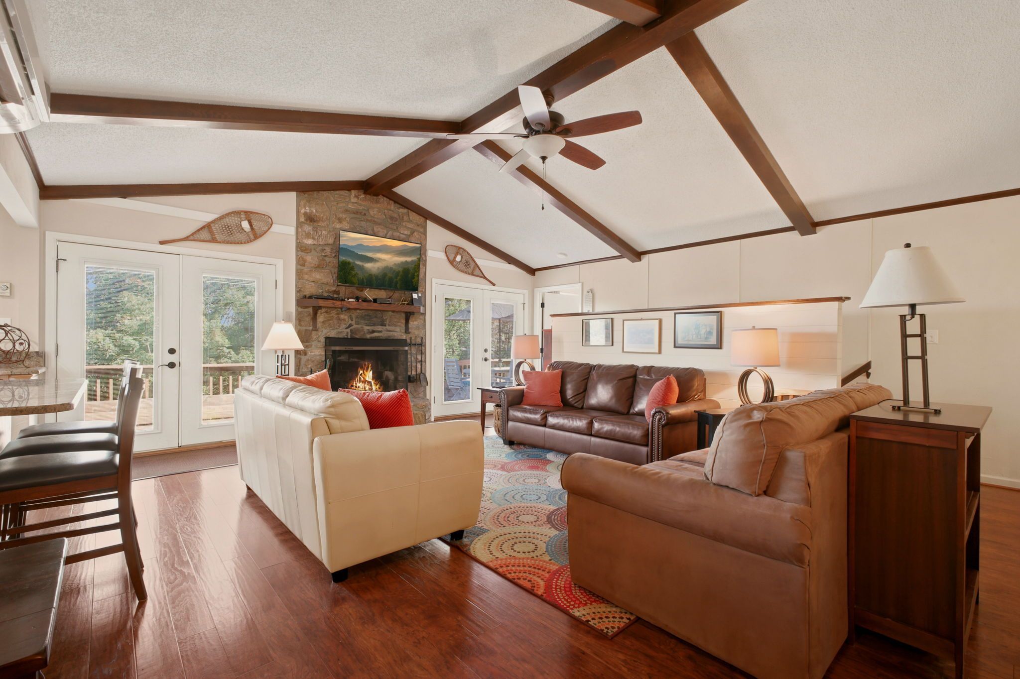 A spacious living room with a fireplace, a ceiling fan, and a large window.