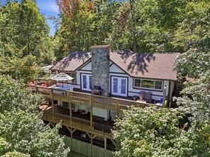 A two-story house with a stone chimney, a deck with outdoor furniture, and a fire pit. - La Shika Chalet | Dogs Welcome | Sleeps 12 (Beech Mountain)
