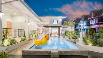 A swimming pool with a rubber duck, surrounded by greenery and a building with a balcony.
