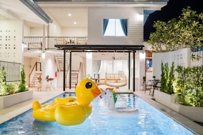 An indoor swimming pool with inflatable toys, a staircase, and indoor plants.