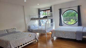 A room with two beds, a bunk bed, and a window with a view of greenery.