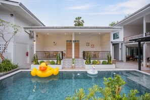 A swimming pool with two inflatable toys, a covered patio area with seating, and a view of the surrounding buildings.