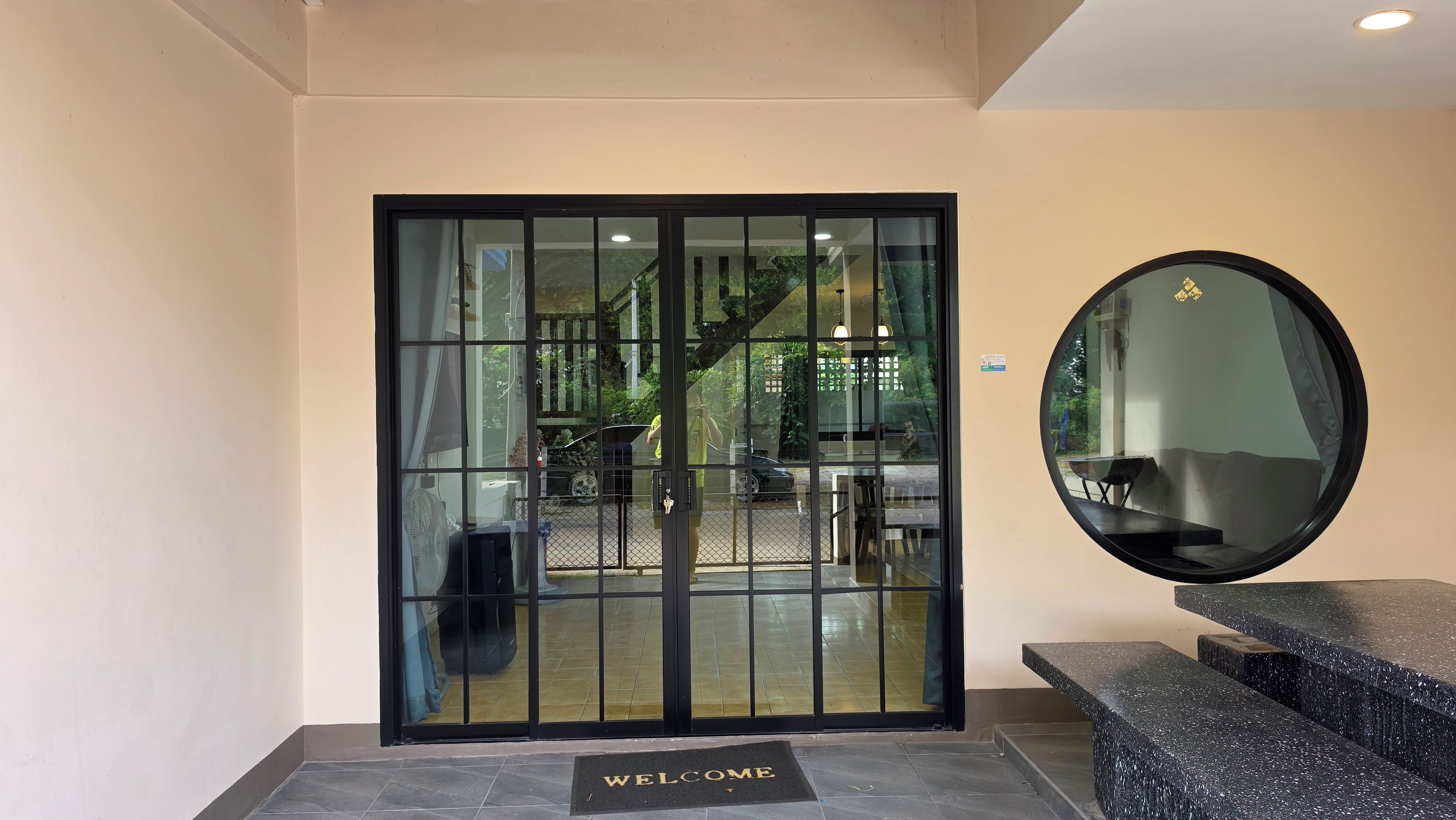 A hotel entrance with a glass door, a welcome mat, a round mirror, and a staircase leading to the upper floors.