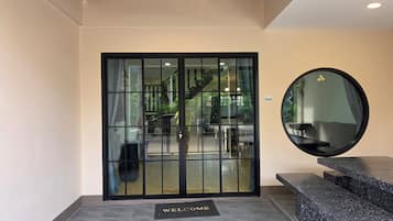 A hotel entrance with a glass door, a welcome mat, a round mirror, and a staircase leading to the upper floors.