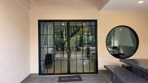 A hotel entrance with a glass door, a welcome mat, a round mirror, and a staircase leading to the upper floors.