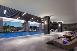 A modern indoor pool area with lounge chairs and a view of traditional architecture outside.