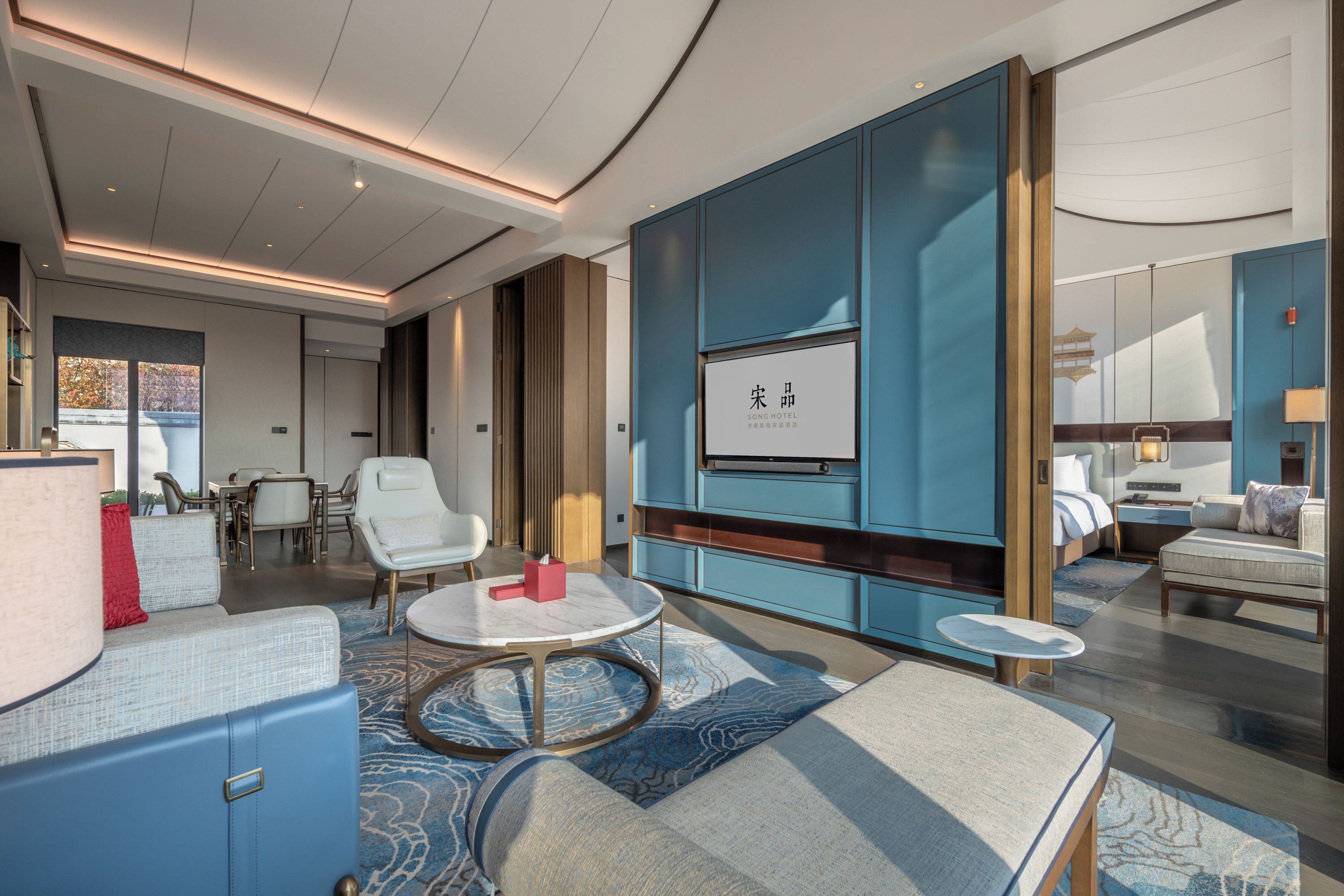 A modern hotel room with a large bed, a seating area with a coffee table, and a television mounted on the wall.
