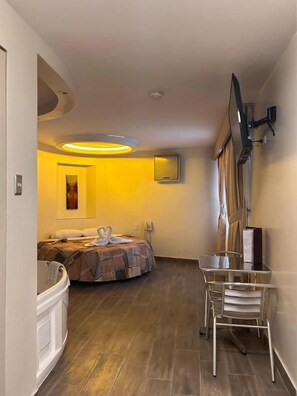 Habitación de hotel con cama, escritorio, silla, televisor de pantalla plana montado en la pared y lámpara del techo.
