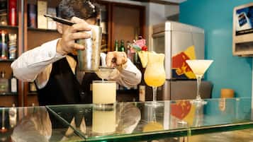A bartender preparing drinks behind a bar with various bottles and a refrigerator in the background.
