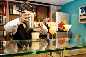 A bartender preparing drinks behind a bar with various bottles and a refrigerator in the background. - Los Mirtos Suite & Hotel (Lima)