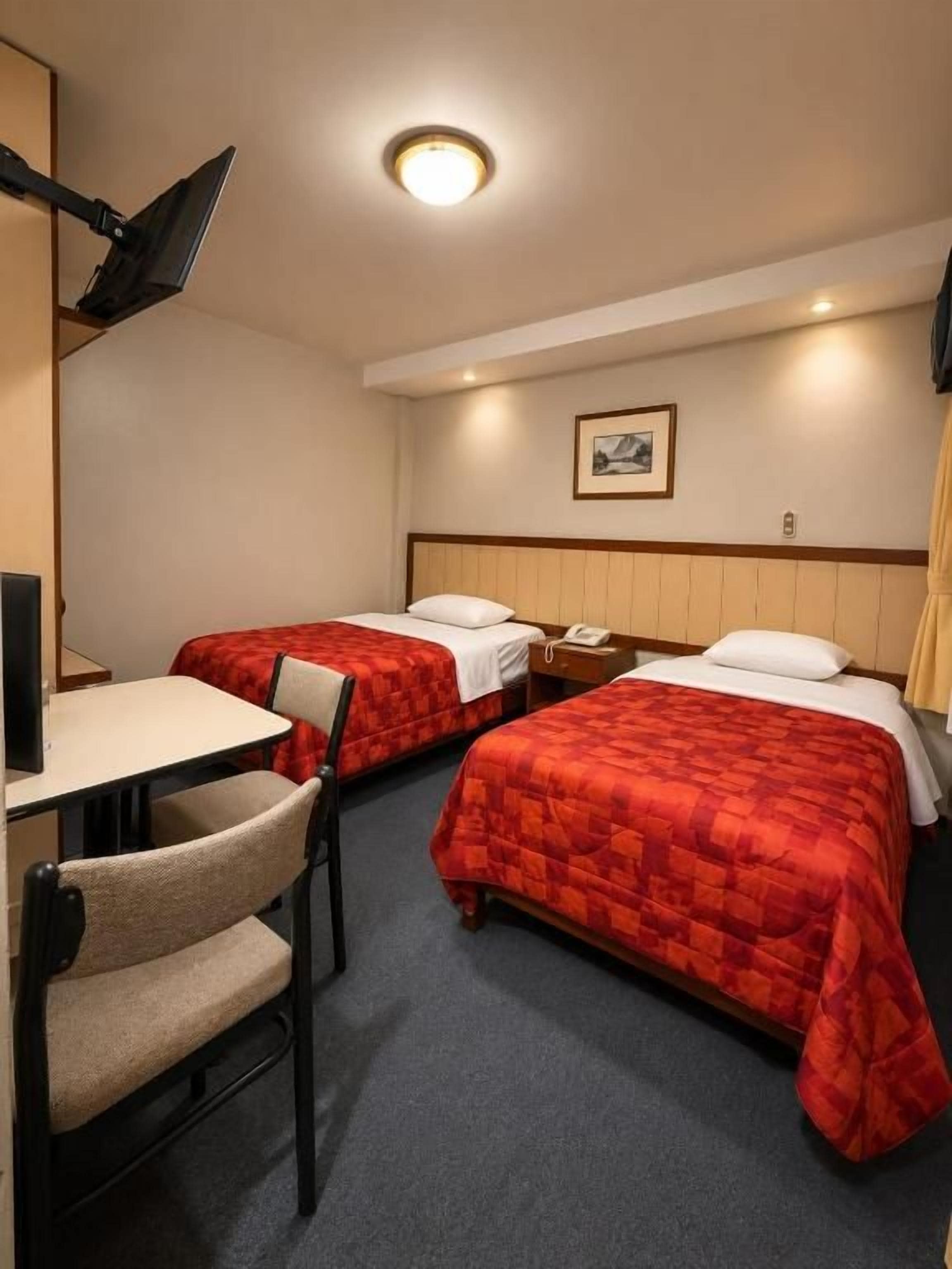 Una habitación de hotel con dos camas, un escritorio, una silla y una lámpara.