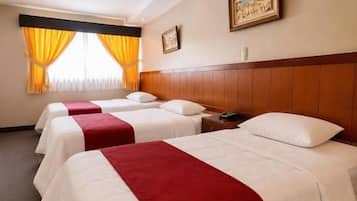 A hotel room with three beds, each with a red and white bedspread, a wooden headboard, and a painting on the wall.