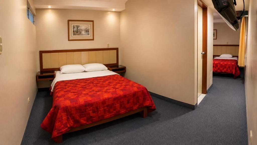 Habitación de hotel con cama, mesita de noche, un cuadro colgado en la pared y una puerta que da a otra habitación.