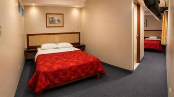 Habitación de hotel con cama, mesita de noche, un cuadro colgado en la pared y una puerta que da a otra habitación.
