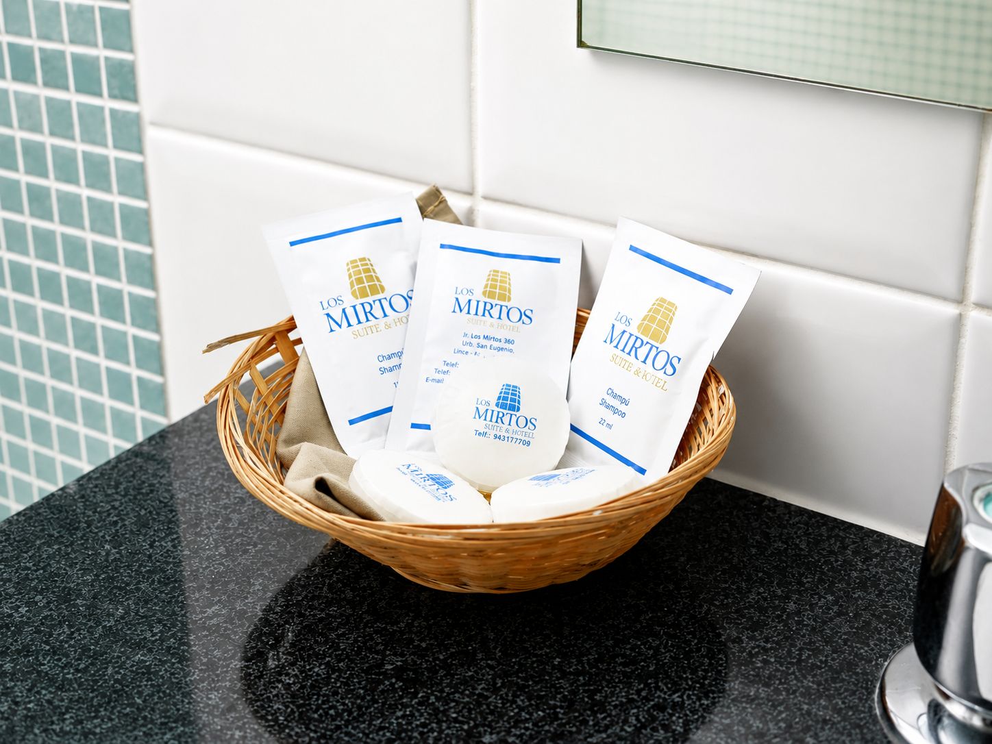 A wicker basket containing three white bags with blue text and a logo, placed on a black countertop.