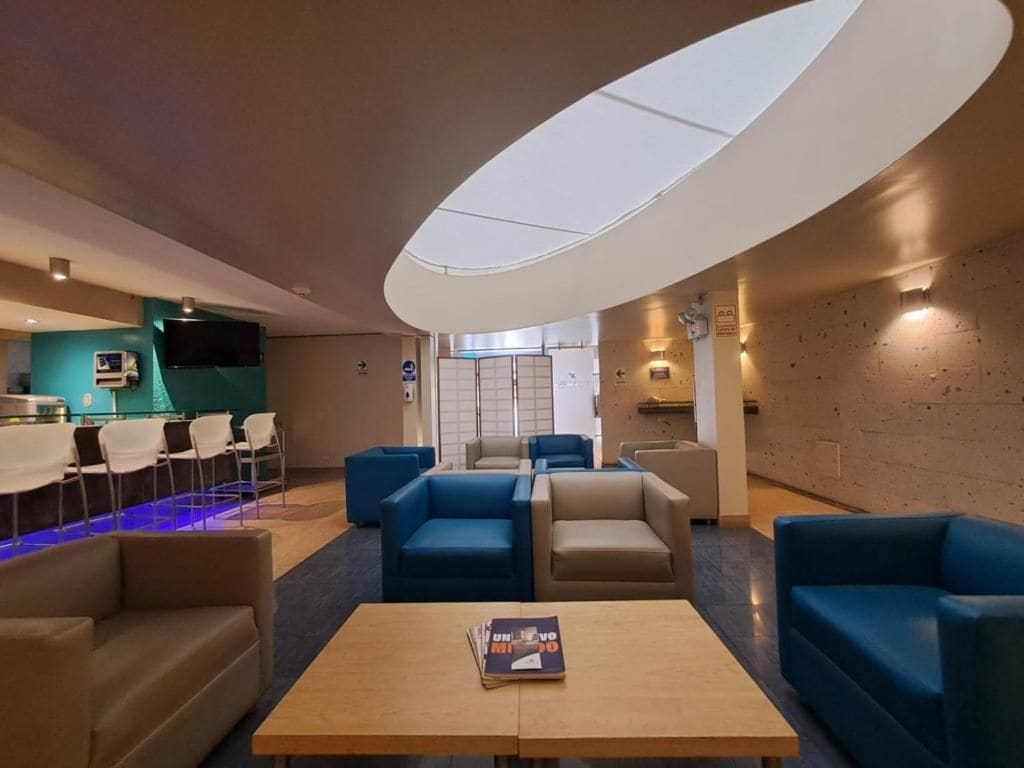 Un área de estar moderna con asientos y una mesa central, un televisor montado en la pared y un tragaluz grande.