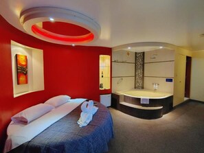 A hotel room with a bed, a large bathtub, and a red accent wall. - Los Mirtos Suite & Hotel (Lima)