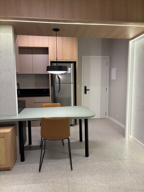 Una cocina moderna con refrigerador empotrado, una mesa de comedor con sillas y una lámpara colgante.