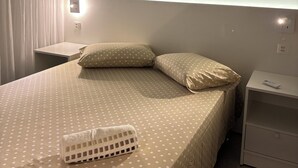 Ein Schlafzimmer mit einem Bett, einem Nachttisch, einer Fernbedienung und einer wandmontierten Leuchte.