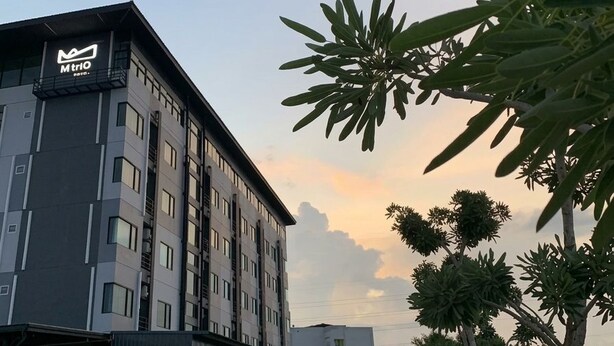 A modern hotel building with a sign 'Mtrio' and a parking area with a car. - Mtrio Hotel Korat (Nakhon Ratchasima)