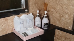 Ein Badezimmer mit Marmorwand, schwarzem Waschtisch, einem Waschbecken und Pflegeprodukten, darunter ein Haarkonditionierer und Körperlotion.