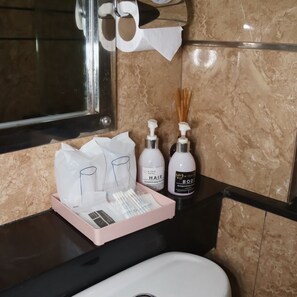 A bathroom with a marble wall, a black countertop, a sink, and toiletries including a hair conditioner and body lotion. - Mtrio Hotel Korat (Mueang Nakhon Ratchasima)