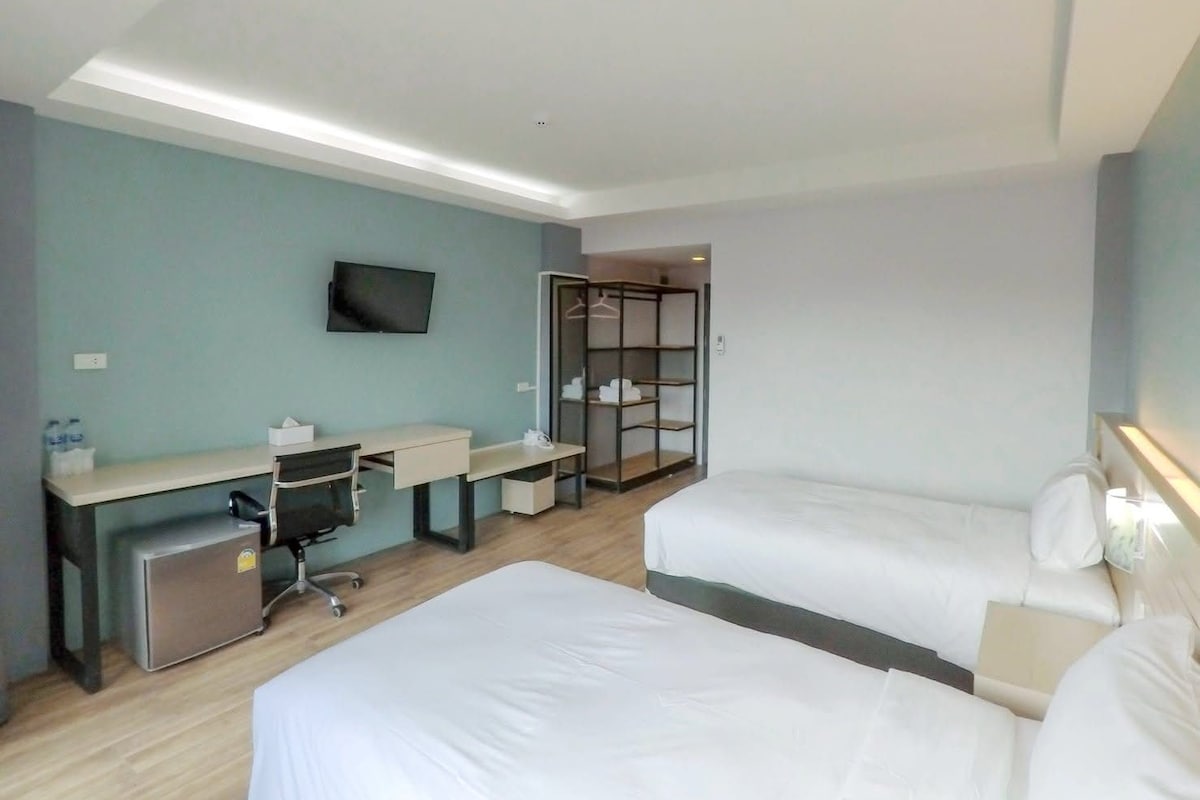 A hotel room with a desk, two beds, a TV, and a walk-in closet.