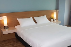 A hotel room with a bed, two bedside tables, and a nightstand with a lamp. - Mtrio Hotel Korat (Mueang Nakhon Ratchasima)