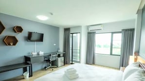 Ein Hotelzimmer mit einem Bett, einem Schreibtisch, einem Stuhl, einem Fernseher und einem Fenster mit Vorhängen.