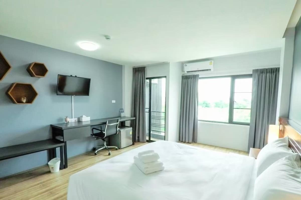 A hotel room with a bed, a desk, a chair, a TV, and a window with curtains.