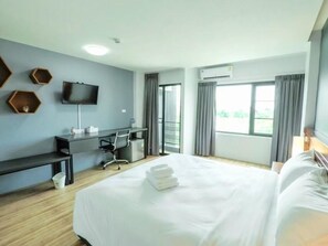 A hotel room with a bed, a desk, a chair, a TV, and a window with curtains. - Mtrio Hotel Korat (Mueang Nakhon Ratchasima)