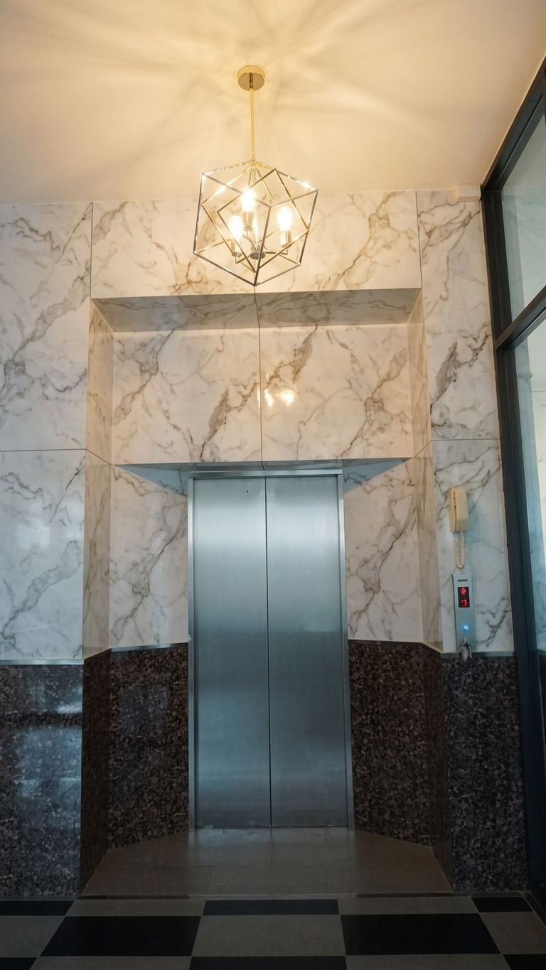A modern elevator with marble walls and a geometric light fixture.
