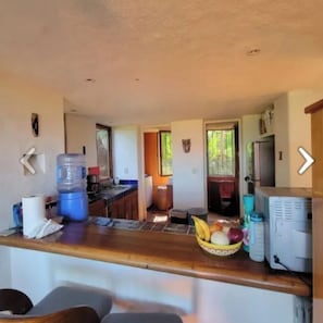 A kitchen with a large water dispenser, a fruit bowl, and a refrigerator.