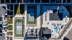 Ein Luftbild eines Anwesens mit Tennisplatz, Poolbereich inklusive Liegestühlen und einem Parkplatz.