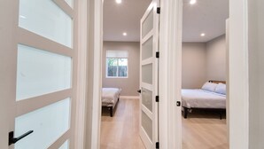 A hallway leading to two bedrooms with a window and a door with frosted glass panels. - Modern 2BR/2BA Guest House in Granada Hills (Los Angeles)