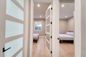 A hallway leading to two bedrooms with a window and a door with frosted glass panels. - Modern 2BR/2BA Guest House in Granada Hills (Los Angeles)