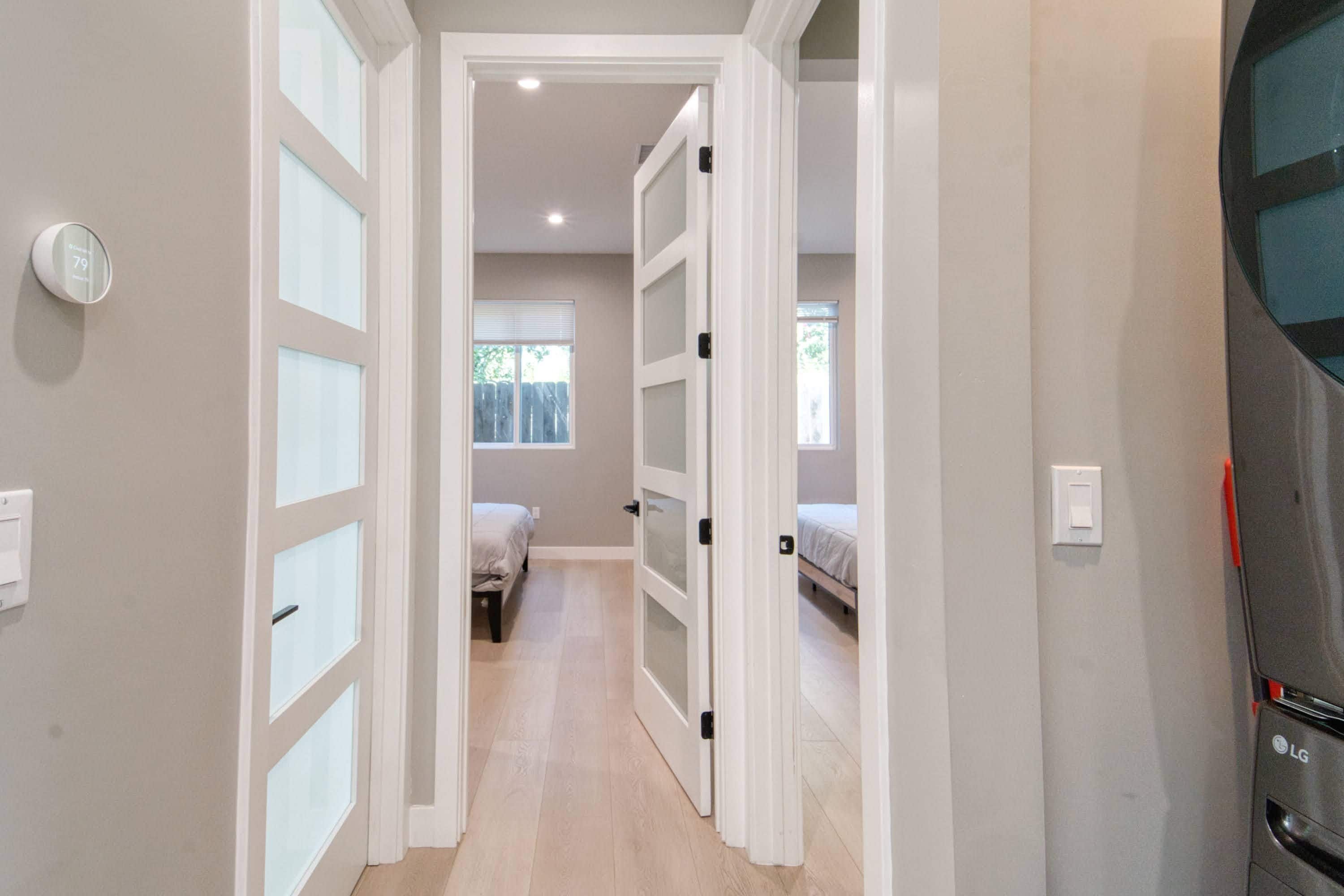 A hallway with a door leading to a bedroom with a bed and a window.
