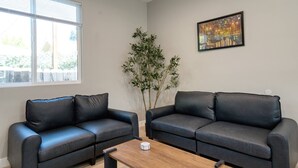 A modern living room with two black leather sofas, a wooden coffee table, a large window, and a painting on the wall. - Modern 2BR/2BA Guest House in Granada Hills (Los Angeles)