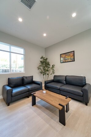 A modern living room with two black leather sofas, a wooden coffee table, a large window, and a painting on the wall. - Modern 2BR/2BA Guest House in Granada Hills (Los Angeles)