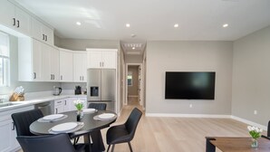 A modern kitchen with white cabinets, a stainless steel refrigerator, and a dining area with a table set for four. - Modern 2BR/2BA Guest House in Granada Hills (Los Angeles)