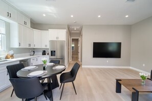 A modern kitchen with white cabinets, a stainless steel refrigerator, and a dining area with a table set for four. - Modern 2BR/2BA Guest House in Granada Hills (Los Angeles)
