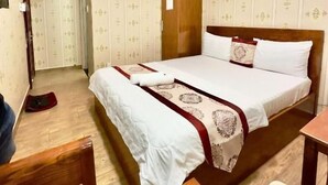 A hotel room with a bed, a wooden chair, a table, an air conditioning unit, and a wardrobe. - DŨNG INDIA HOTEL (Tân Bình)