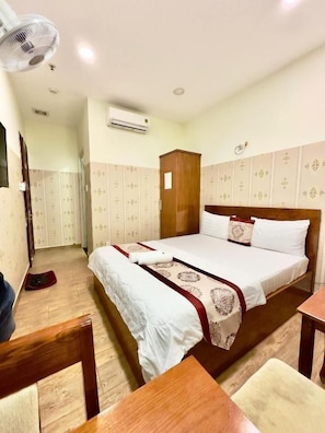 A hotel room with a bed, a wooden chair, a table, an air conditioning unit, and a wardrobe. - DŨNG INDIA HOTEL (Tân Bình)
